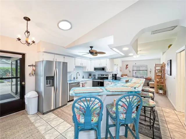 Kitchen with lofted ceiling, stainless steel appliances, ceiling fan with notable chandelier, and light tile patterned floors
