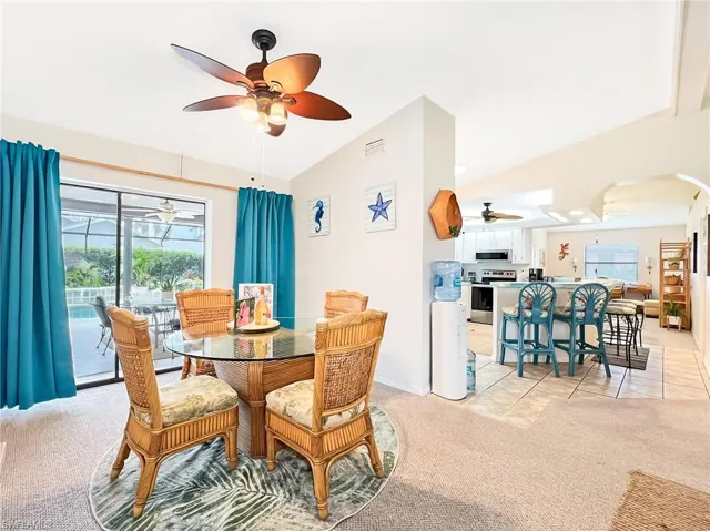 Dining room with ceiling fan, light colored carpet, and lofted ceiling