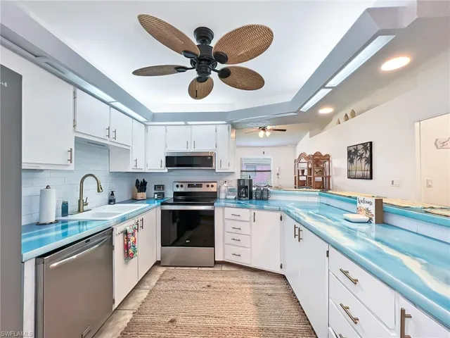 Kitchen with light tile patterned floors, appliances with stainless steel finishes, white cabinets, ceiling fan, and sink