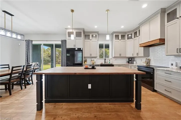 Spacious open-concept kitchen featuring a large wood-finish island, light-toned upper cabinetry, dark lower cabinetry, and wood-finish flooring