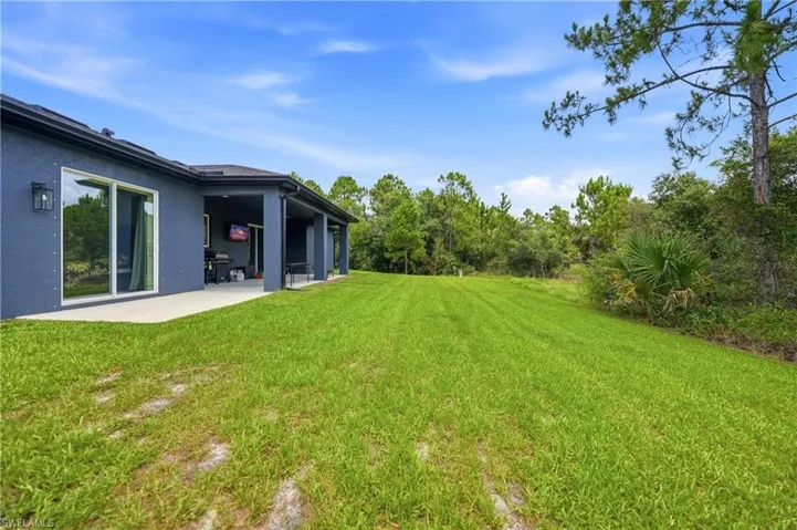 Expansive green lawn with a covered patio, large sliding glass door, and exterior wall sconce