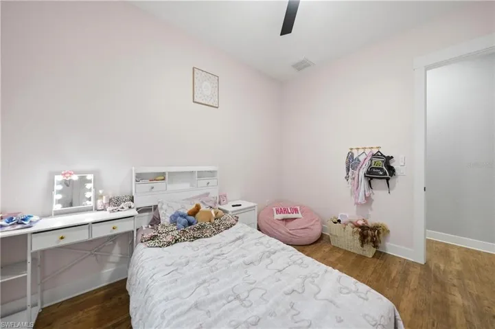 Wood-finish flooring extends throughout this room, featuring a white built-in headboard with integrated storage