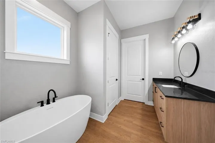 Freestanding soaking tub with a black matte faucet, wood-finish flooring, and light gray walls
