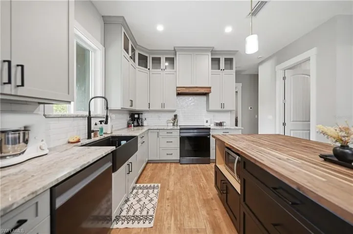 Modern kitchen featuring light gray cabinetry, wood-finish flooring, a butcher block island, black appliances, and a farmhouse-style sink