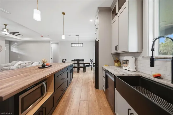 Contemporary kitchen featuring a spacious island with a wood-finish countertop and built-in microwave, light-toned upper cabinetry, dark lower cabinetry, a large black farmhouse sink with a gooseneck faucet, and light-colored wood-finish flooring