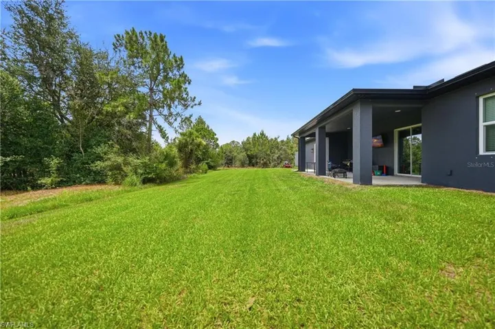 Expansive green lawn bordering a modern dark gray exterior with a covered patio featuring a concrete slab and columns