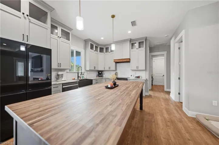 Kitchen featuring an expansive butcher block island, light gray cabinetry with upper glass-front accents, and wood-finish flooring