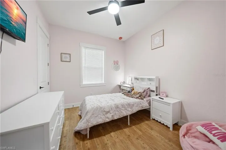 Room featuring wood-finish flooring, a ceiling fan with integrated lighting, and a window with blinds