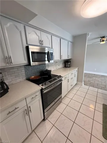 White cabinetry with brushed nickel hardware, stainless steel appliances, light-toned countertops, and a full-height tile backsplash