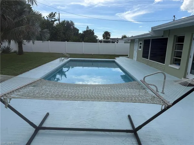 Outdoor pool with a surrounding concrete patio, bordered by a white privacy fence and a manicured lawn