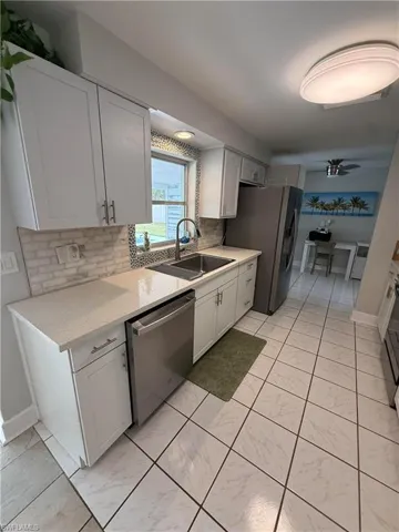 White shaker cabinetry, light-toned countertops, stainless steel appliances, ceramic tile flooring, and mosaic tile backsplash