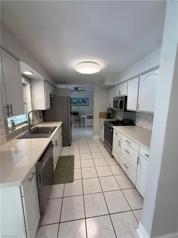 Galley kitchen featuring white cabinetry, light-toned countertops, stainless steel appliances, a tile backsplash, and tile flooring