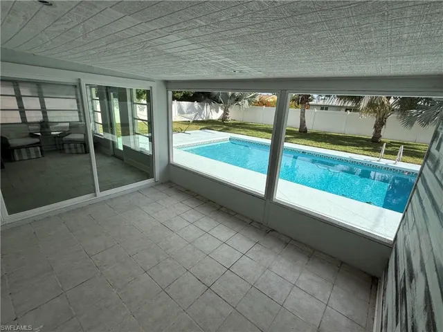 Screened patio with tile flooring, offering direct access to an outdoor swimming pool, surrounded by a manicured lawn and privacy fencing