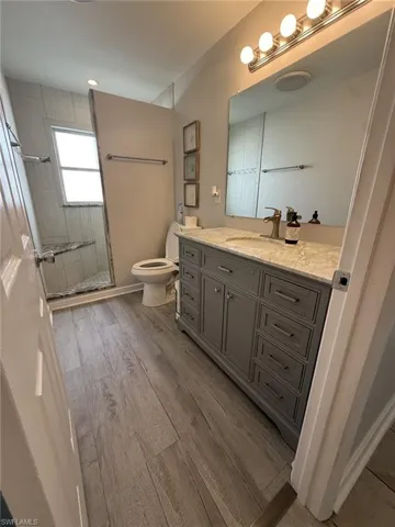 Spacious bathroom featuring a single vanity with a stone countertop, a walk-in shower with tiled walls and a built-in bench, wood-finish flooring, and a large wall-mounted mirror