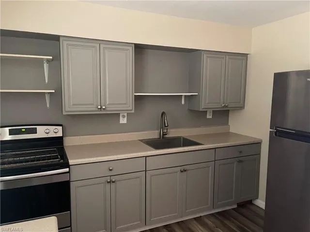 Kitchen featuring open shelves, gray cabinets, appliances with stainless steel finishes, light countertops, and dark wood-style floors