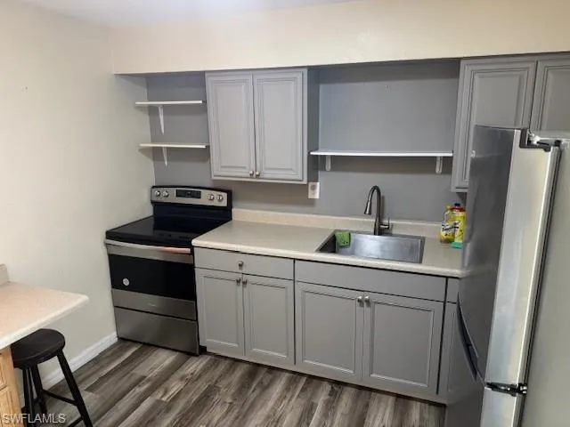 Kitchen with gray cabinetry, open shelves, appliances with stainless steel finishes, and light countertops