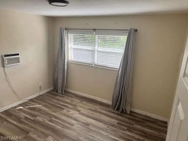 Empty room with dark wood-style floors and a wall mounted AC