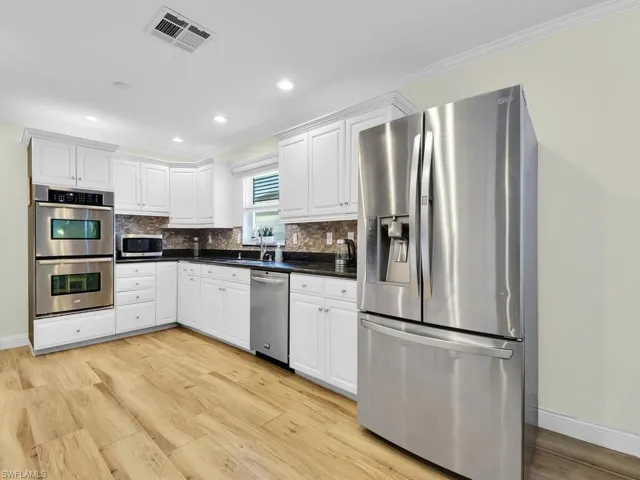 Kitchen with appliances with stainless steel finishes, white cabinets, decorative backsplash, light wood-type flooring, and recessed lighting
