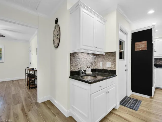 Kitchen with ornamental molding, dark stone countertops, decorative backsplash, white cabinets, and light wood-type flooring