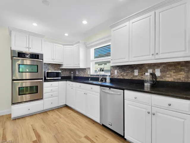 Kitchen with white cabinets, stainless steel appliances, decorative backsplash, light wood-style floors, and recessed lighting