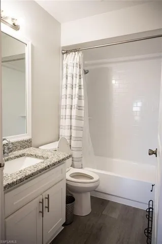 Full bath with vanity, shower / bath combo with shower curtain, and dark wood-type flooring