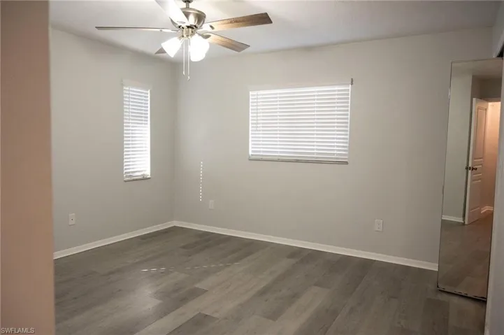 Unfurnished room with dark wood-style floors, healthy amount of natural light, and ceiling fan