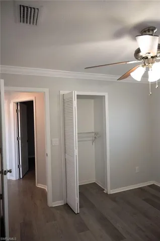 Unfurnished bedroom featuring dark wood finished floors, a closet, ornamental molding, and a ceiling fan