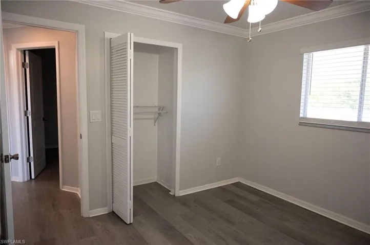 Unfurnished bedroom featuring crown molding, a closet, dark wood-style floors, and a ceiling fan