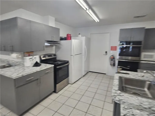Kitchen with stainless steel appliances, gray cabinets, and light stone counters