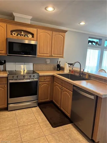 Kitchen with stainless steel appliances, ornamental molding, light countertops, light tile patterned floors, and a peninsula