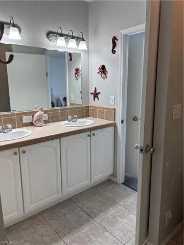 Bathroom with double vanity, light tile patterned flooring, and backsplash
