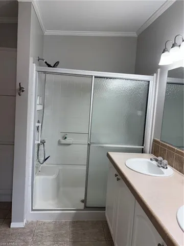 Bathroom with ornamental molding, a stall shower, double vanity, and light tile patterned floors