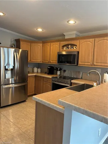 Kitchen featuring stainless steel appliances, crown molding, light countertops, recessed lighting, and wood finish cabinetry