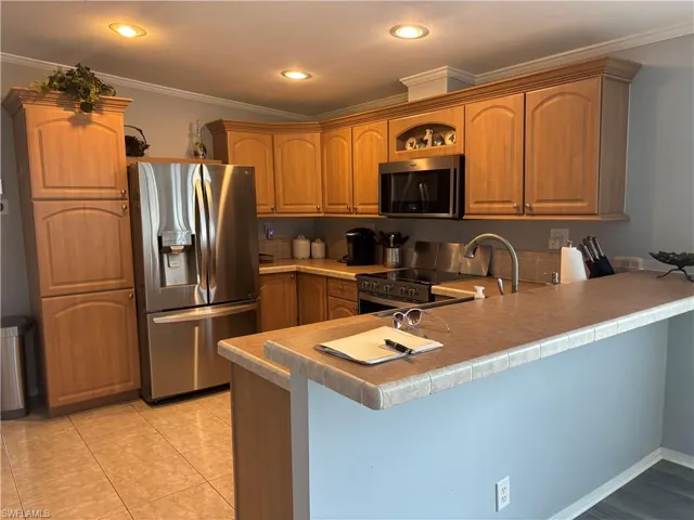 Kitchen with a peninsula, stainless steel appliances, ornamental molding, recessed lighting, and light countertops