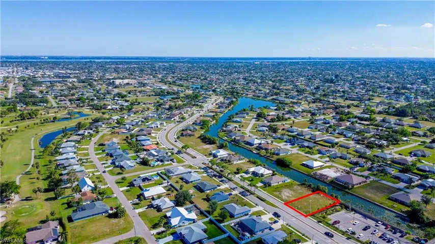 Aerial view of property's location featuring property parcel outlined, a nearby body of water, nearby suburban area, and a local golf course