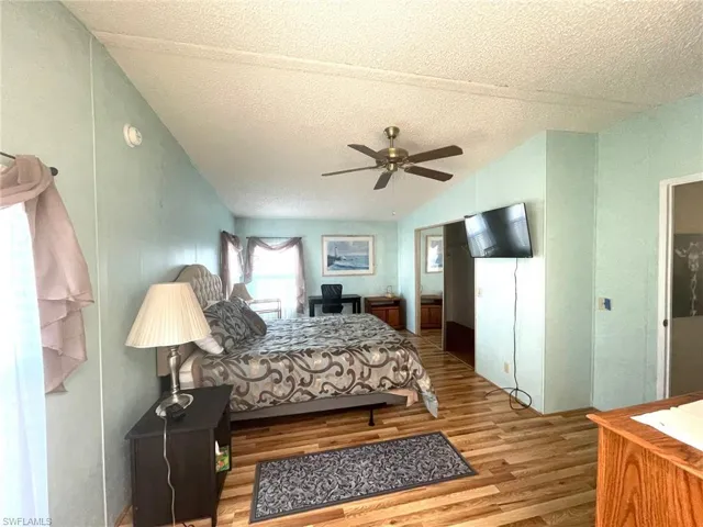 Bedroom with lofted ceiling, wood finished floors, a textured ceiling, and a ceiling fan