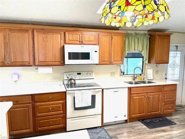 Kitchen featuring white appliances, a textured ceiling, brown cabinets, light wood finished floors, and light stone counters