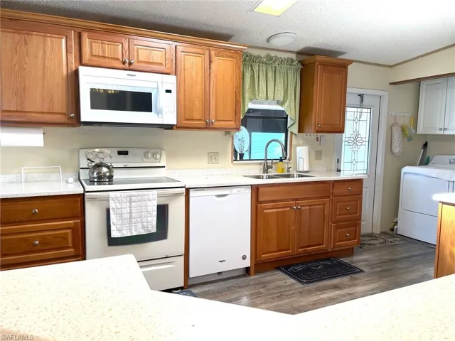 Kitchen featuring brown cabinets, white appliances, washer / dryer, a textured ceiling, and crown molding