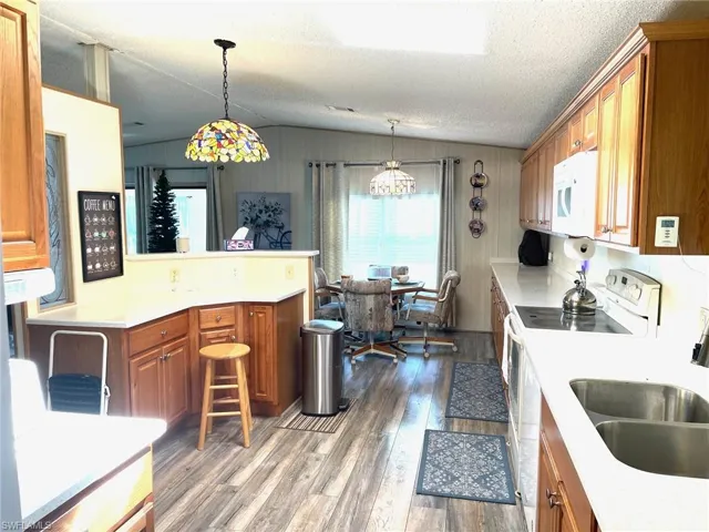 Kitchen with brown cabinetry, decorative light fixtures, a peninsula, dark wood-type flooring, and white appliances