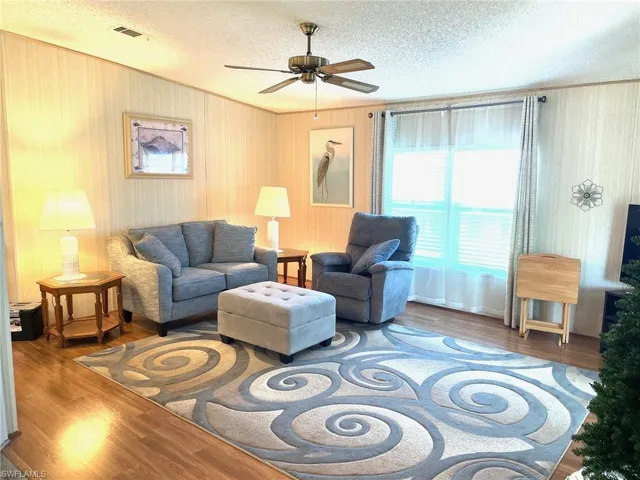 Living room featuring wood finished floors, a textured ceiling, a ceiling fan, and crown molding
