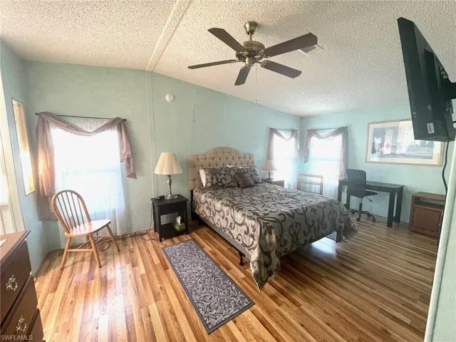 Bedroom with lofted ceiling, light wood-style flooring, a textured ceiling, and ceiling fan