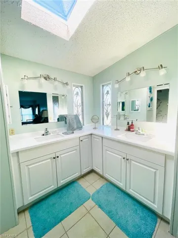 Bathroom featuring a textured ceiling, light tile patterned floors, a skylight, and double vanity