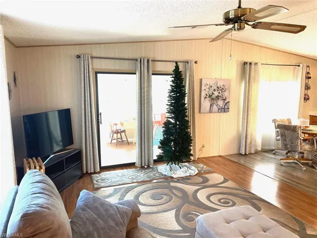 Living room with a textured ceiling, wood finished floors, ceiling fan, and vaulted ceiling