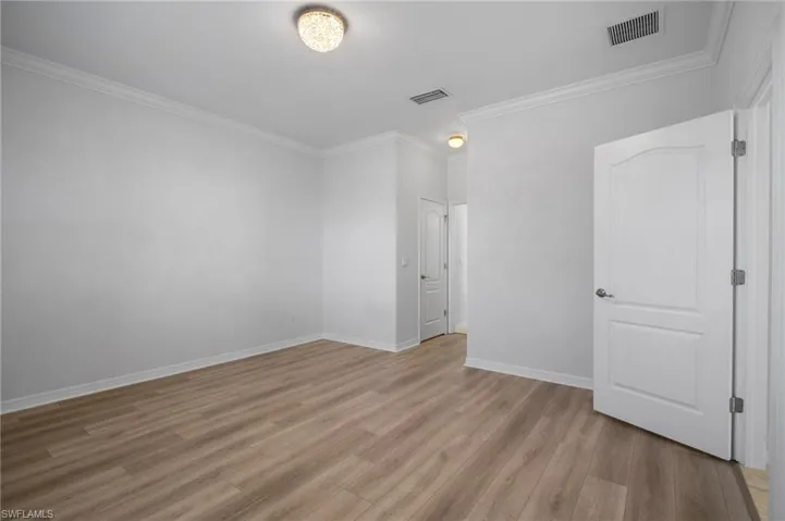 Empty room featuring ornamental molding, baseboards, visible vents, and light wood finished floors