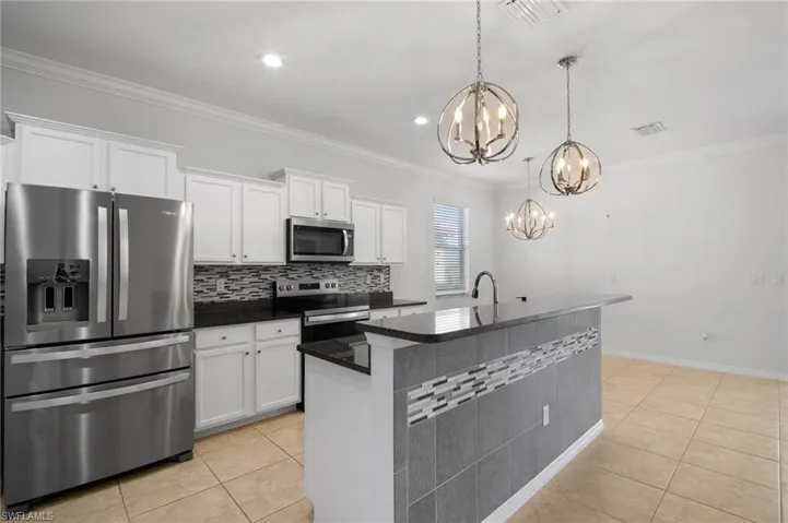 Kitchen with a kitchen island with sink, stainless steel appliances, visible vents, white cabinets, and decorative light fixtures