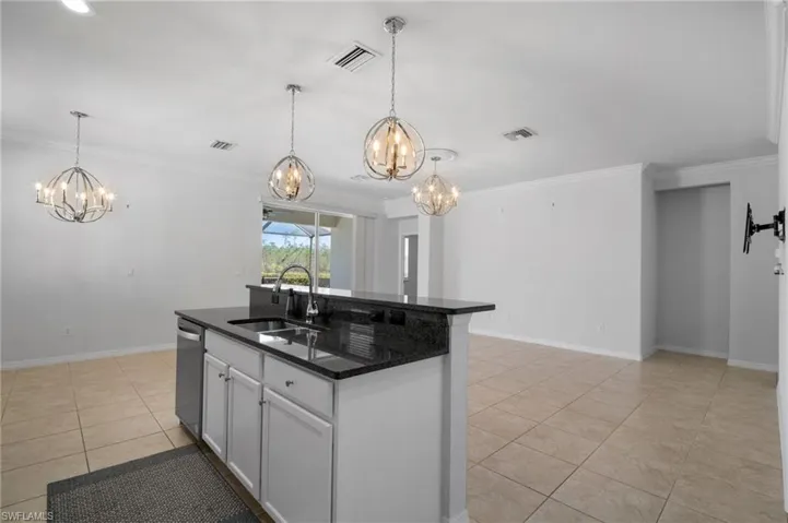 Kitchen with light tile patterned flooring, a sink, hanging light fixtures, dishwasher, and an island with sink