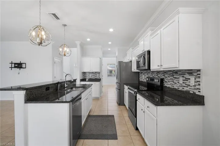 Kitchen featuring stainless steel appliances, a sink, white cabinetry, an island with sink, and pendant lighting