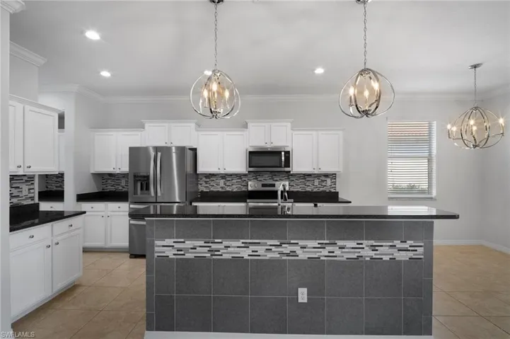 Kitchen featuring stainless steel appliances, an island with sink, dark countertops, and decorative light fixtures