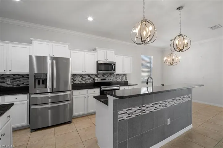 Kitchen with appliances with stainless steel finishes, a kitchen island with sink, white cabinetry, and decorative light fixtures