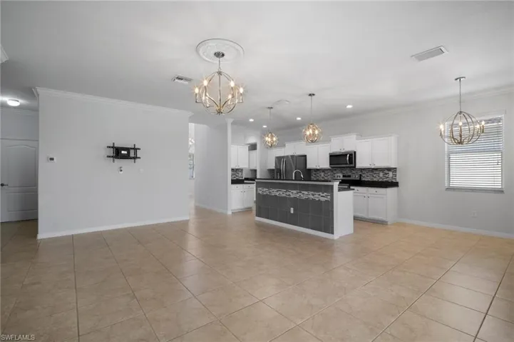 Kitchen featuring appliances with stainless steel finishes, dark countertops, white cabinets, and a notable chandelier